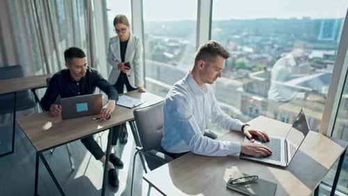 Office employees working in a sunny modern office. Men sitting at desk in front of laptops.