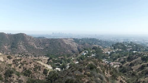 Inclinación aérea ligeramente ascendente sobre Hollywood Hill, con Los Ángeles apenas visible en la bruma de la h