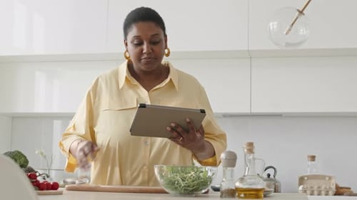 Woman Prepares Food in Bright Kitchen with Tablet