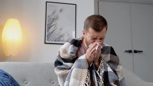 Man Sneezing With A Cold Wrapped in Blanket