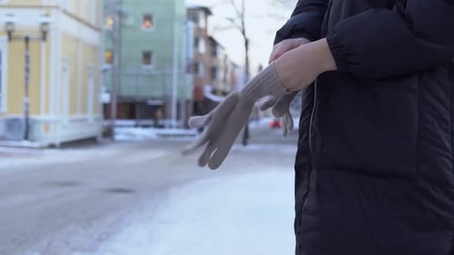 Woman putting on gloves in cold winter weather on a snowy city street