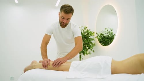 Massage Therapist Performs Leg Massage for Woman in Spa
