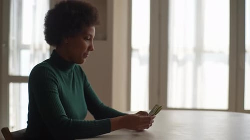 Side Dramatic View of Frustrated AfricanAmerican Young Woman Holding Counting Dollar Banknotes at