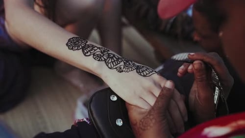 Woman applies henna tattoo to young adult's arm