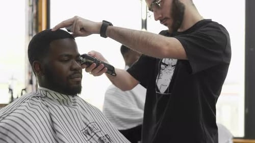 Barber cutting the hair of a young black man in a barbershop studio. Professional hairdresser cuttin