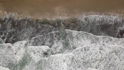 Stormy sea with waves breaking, white foam and beach sand dragged into the sea