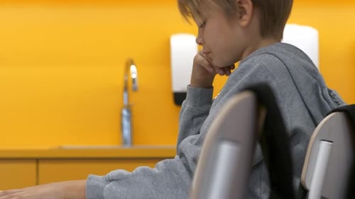 Isolated school boy with tablet sitting at desk in class, raising hand, static side shot