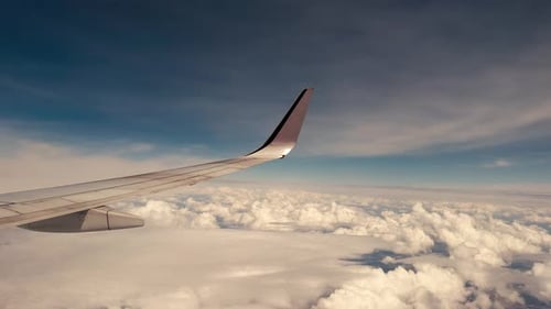 regarder par la fenêtre d'un avion une aile d'avion avec un ciel bleu clair et des nuages en dessous