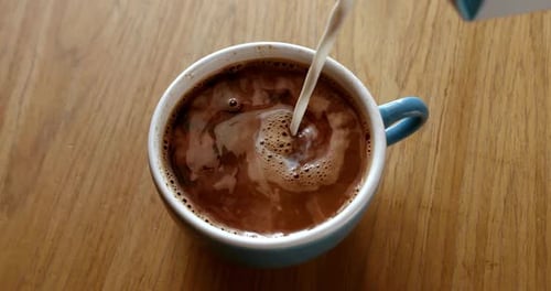 Milk Flowing into Coffee in a Blue Cup