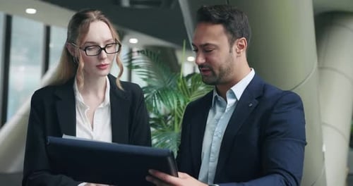Businessman and businesswoman discussing business plan while reviewing statistics in modern office