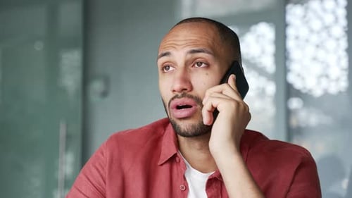 Confident businessman talking on mobile phone while sitting at workplace in modern office. Manager