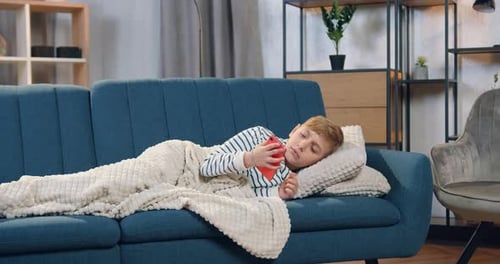 Boy Talking on Phone Lying on Blue Sofa