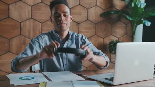 Young African American Man Office Worker Puts on Headphones to Listen to Podcast