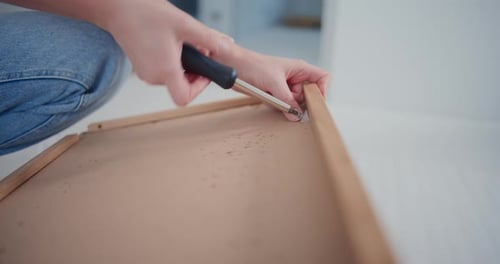 Woman assembling furniture using a screwdriver indoors
