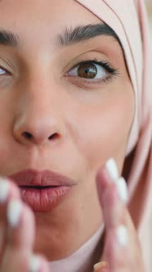 Aufgeregt, überraschte indische Muslima, schockiert, schaut zu Hause in rosafarbenem Hijab in die Kamera und lächelt