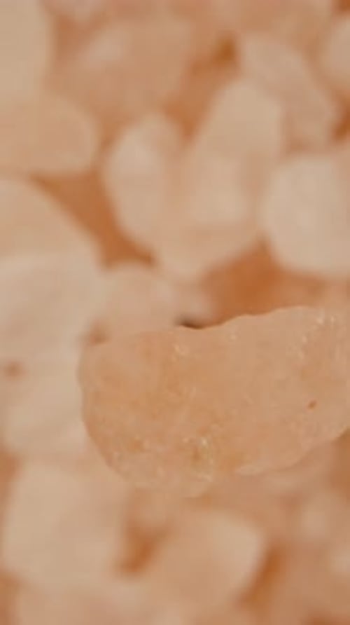 A small grain of pink sea salt falling onto a cluster of salt, macro zoom, top-down view. Vertical