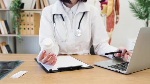 Doctor Using Laptop Holding Medication Bottle