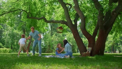 Cheerful family enjoying carefree summer picnic day on green park meadow