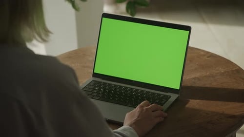Person Using Laptop with Green Screen at a Round Table