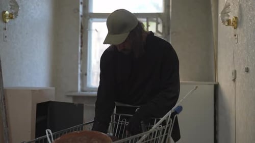 Homeless Man Standing is the Room of an Abandoned Building Searching for Useful Things in a Shopping