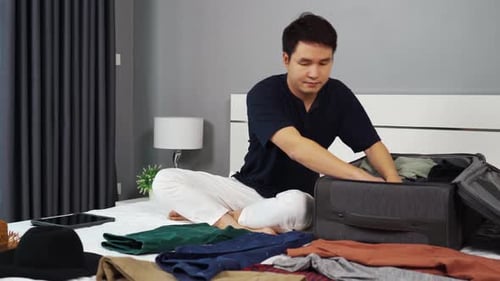 Man packs clothing into suitcase on bed