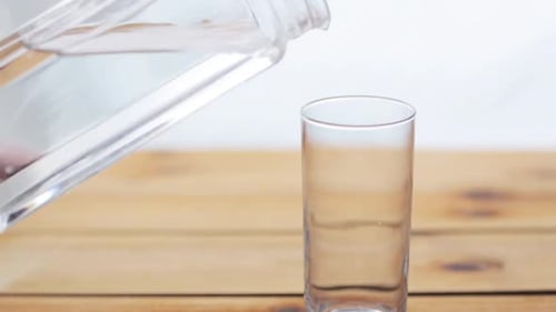 Pouring clear water into drinking glass on wood