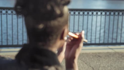 Woman putting on blush and looking on a mirror while sitting on a bench. Shot from behind.