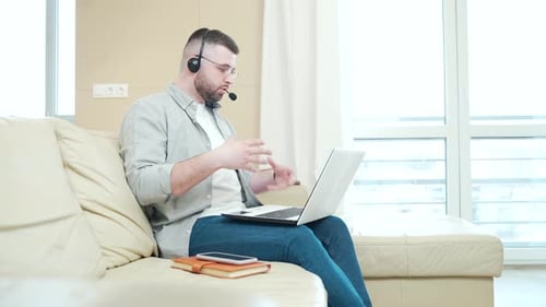 Man in Headset Using Laptop on Couch