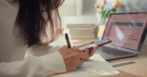 Woman Writes in Notebook While Holding Phone