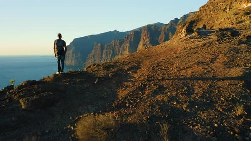 Rear View of Man Hiker Celebrating Climbing to the Top of Mountain Cliff with Ocean Seascape