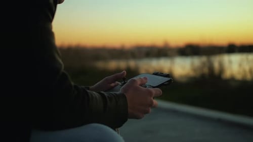 Un piloto masculino concentrado y atractivo que lleva gafas utiliza un mando a distancia con su teléfono inteligente