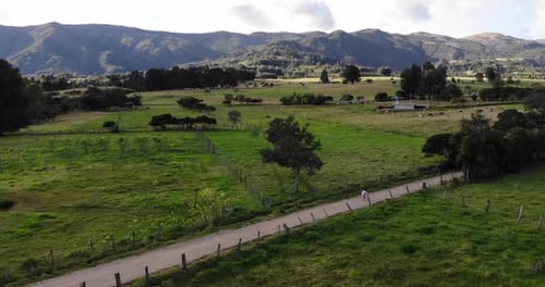 Static aerial shot of a young girl walking her bicycle down a country road