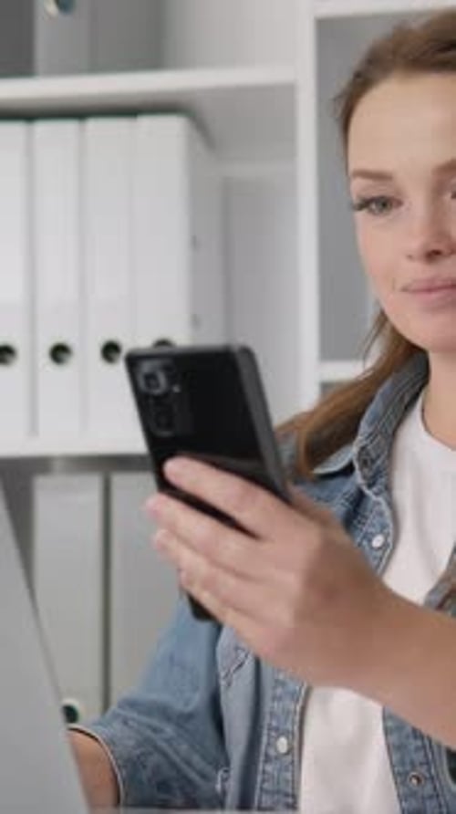 Young Woman Uses Phone and Laptop at Desk