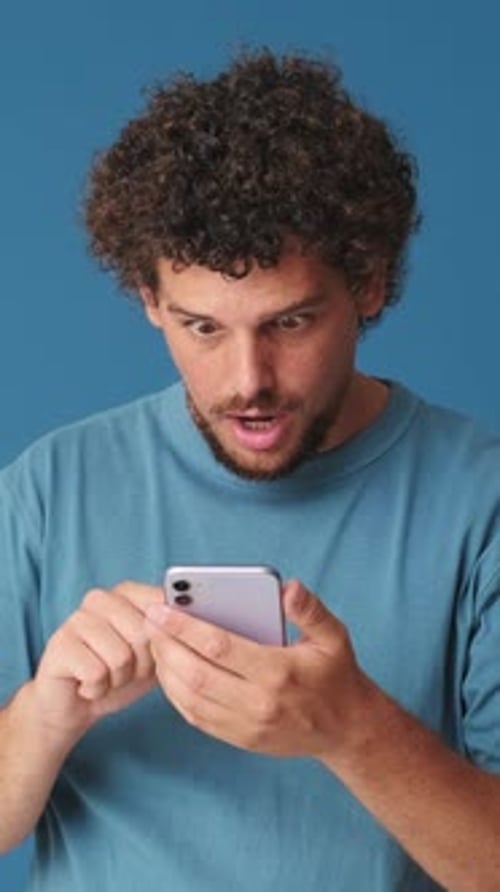 Surprised man with phone in his hands, wow effect in studio on blue background