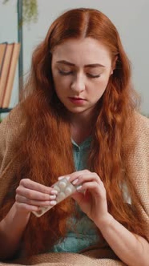 Woman Covered in Blanket Takes Pill With Water