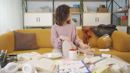Young Woman Sits in Cluttered Room Writing