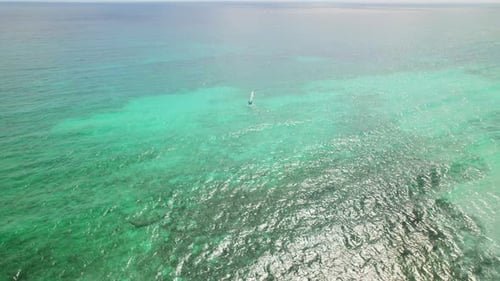Sailboat gliding over bright turquoise Caribbean sea, aerial drone view