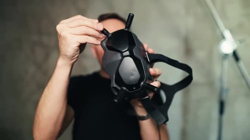 FPV Drone Enthusiast Holds and Wears Modern FPV Goggles Indoors