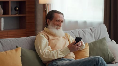 Senior Man Relaxing on Sofa Using Smartphone