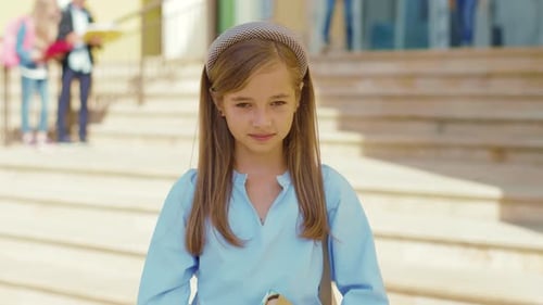 Happy Child Holding Book in Front of School