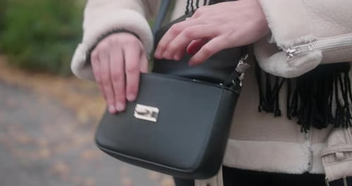Close up of a black purse around a woman's waist wearing a white warm coat. She opens the handbag an