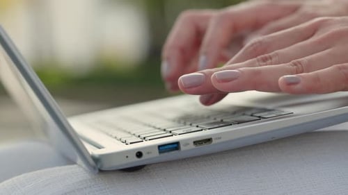 Vue rapprochée de la saisie des mains d'une femme sur un ordinateur portable écrivant un article dans un parc urbain