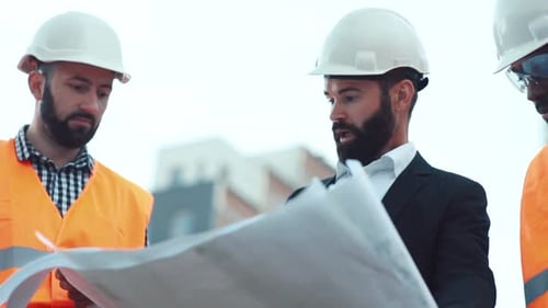 Close Up View of Handsome Bearded Architect in Hard Hat Inspecting the Blueprints with the Finished