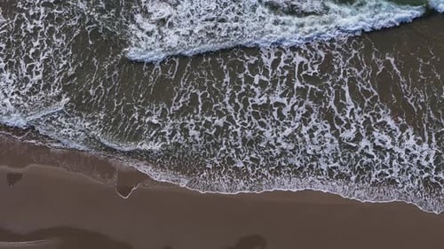 Waves Crashing on Beach Sand from Above