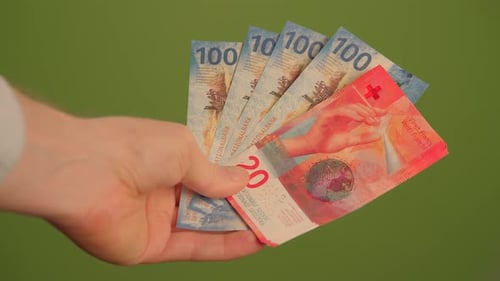 A Hand Grasping Swiss Francs Against a Vibrant Green Background for Visual Appeal