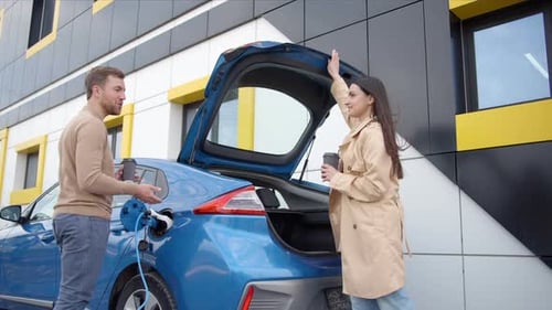 Couple of man and woman install charger plug from charging station to electric car