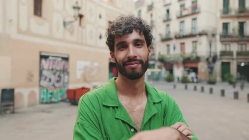 Handsome brunette guy with beard, dressed in green shirt, crosses his arms while looking at camera