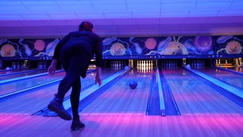 Eine Bowlerin, die in einer neonbeleuchteten Bowlingbahn einen Ball die Bahn entlang wirft, mit einer farbenfrohen Stecknadel
