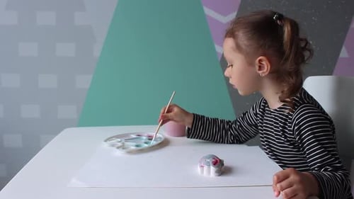Girl Painting a Figurine with Brush at Table
