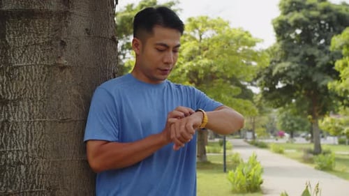 Fit Asian Man Checking Pulse on Fitness Band after Run in Park